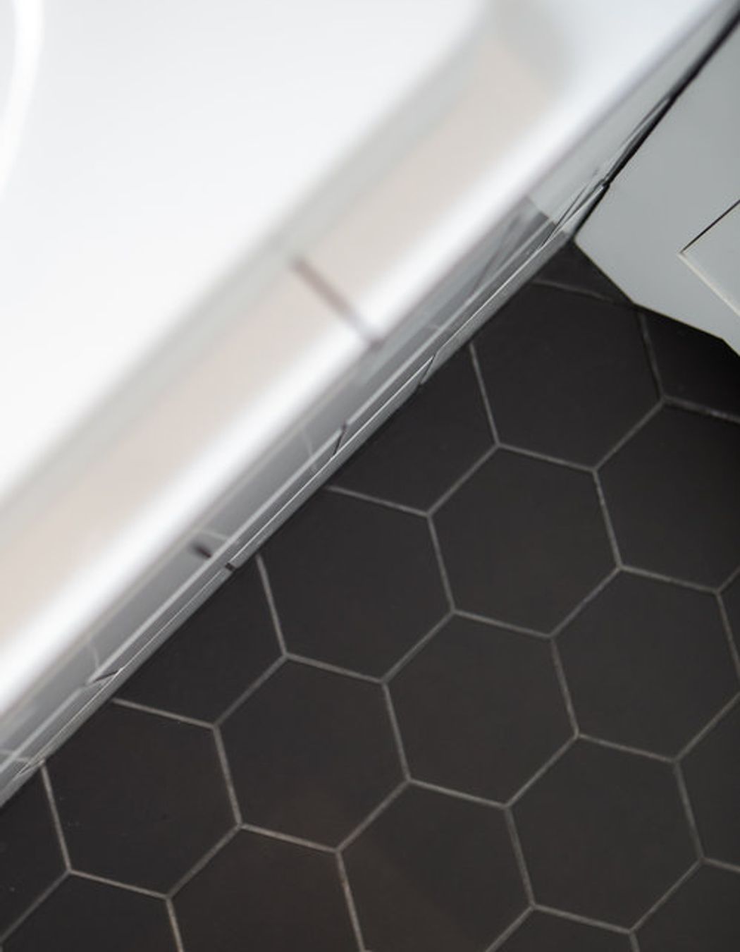 Black hexagonal tiles on the floor are contrasted with gloss white and dark grout on the walls and bath.
