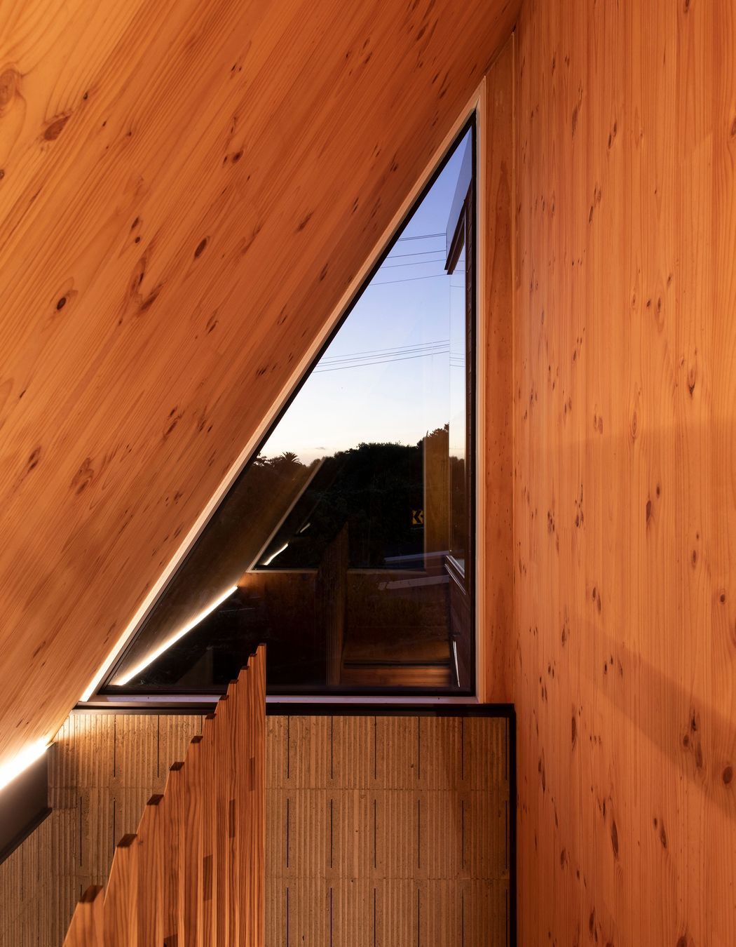 A high triangular window at the top of the stairs is surrounded by New Zealand pine.