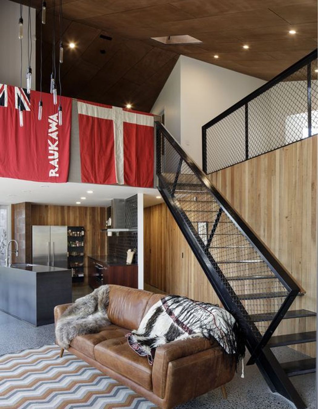 In the kitchen, stained oak-veneer cabinetry is contrasted by black gloss wall tiles, stainless steel appliances and exposed concrete flooring. 