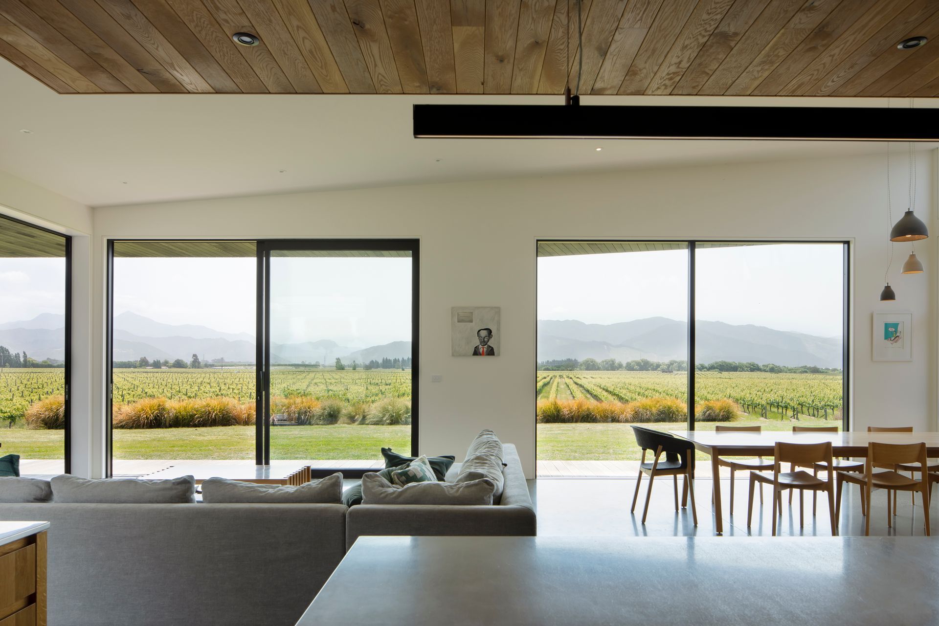 Multiple wide apertures connect the open-plan living area with the view across the valley towards the hills in the distance.