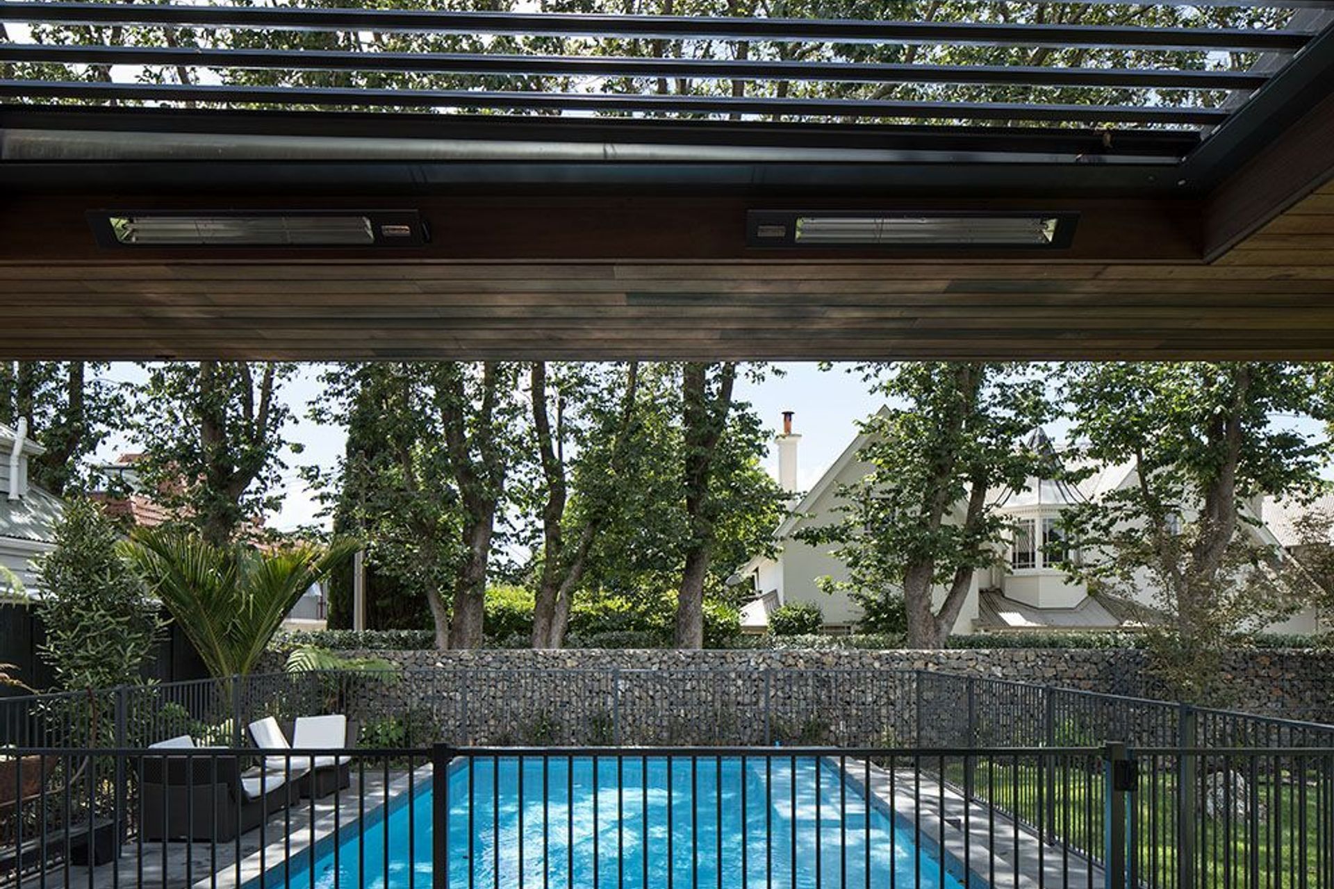 An outdoor room overlooks the swimming pool, mature trees and a gubeon wall filled with volcanic rock excavated from the site prior to the build.