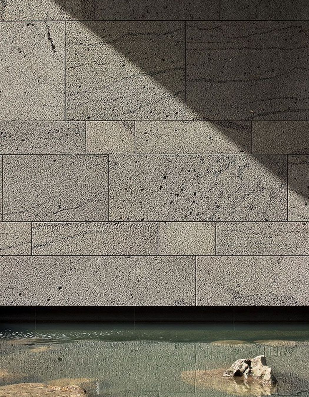 A 'bird-pecked' blue basalt stone wall is reflected in one of the reflection pools.