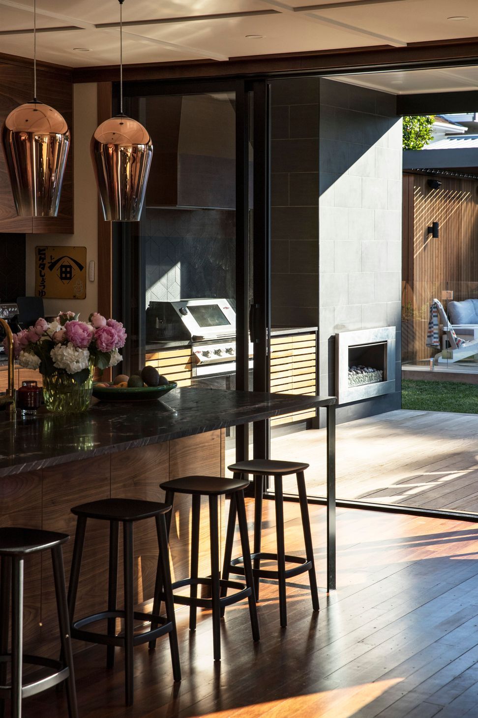 Looking through the open sliding doors, the kitchen extends naturally to a covered outdoor entertaining space complete with a built-in outdoor kitchen and wood-burning fireplace. The carefully planned connection allows entertaining to flow effortlessly between inside and out.
