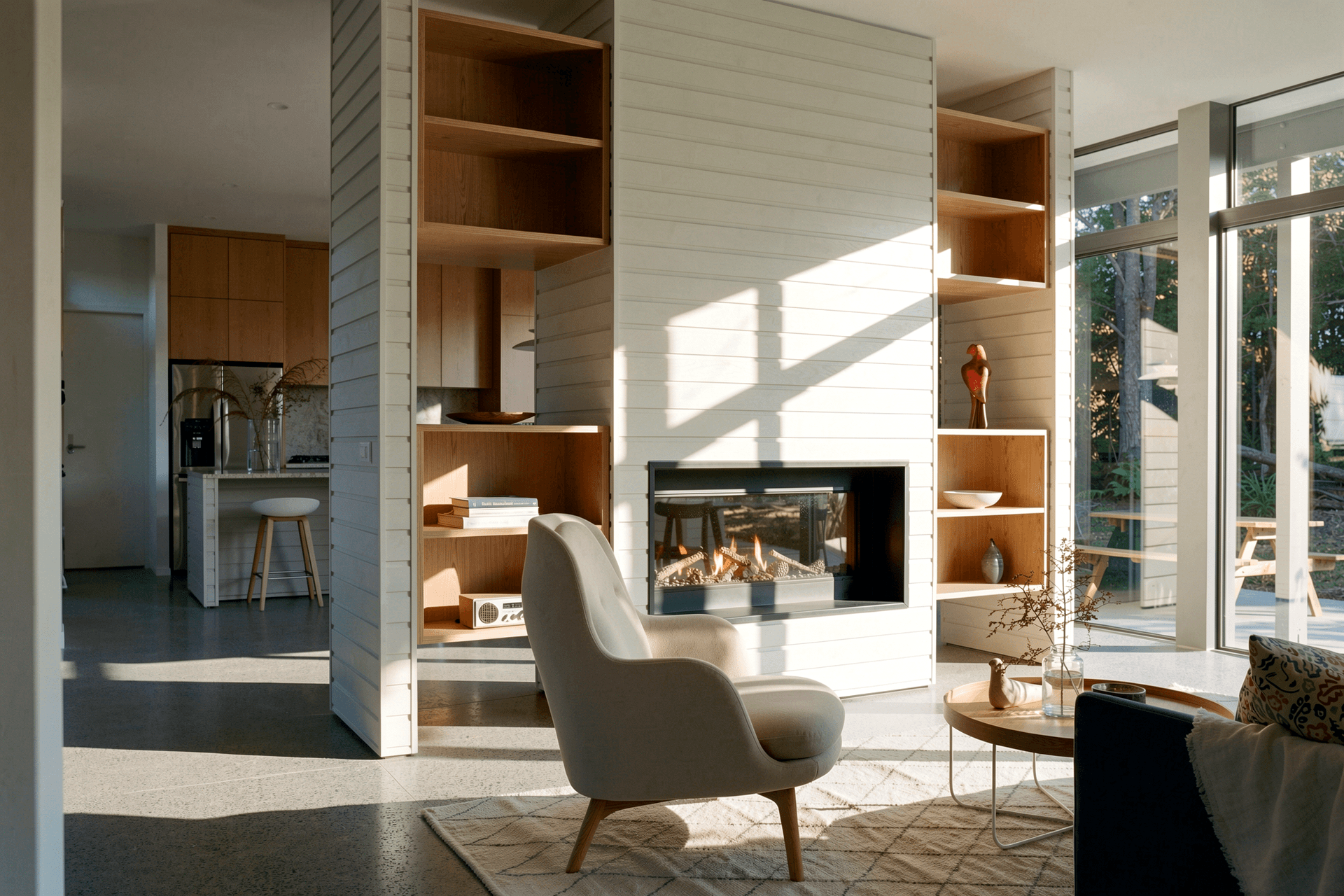 The living room combines comfort with carefully crafted detailing. A HAY About A Lounge chair sits beside the double-sided fireplace, while large grey aluminium sliding doors connect the interior to the sheltered outdoor dining terrace.