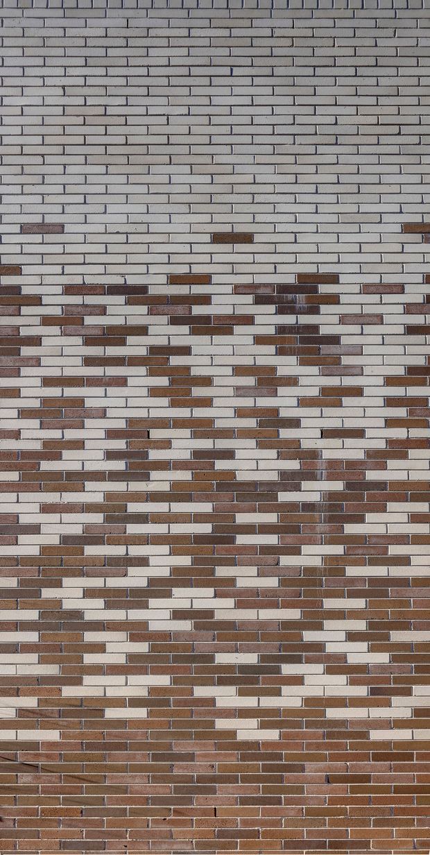 Close-up view of a brick masonry wall composed of narrow horizontal bricks in a running-bond pattern. The upper portion is predominantly pale grey and off-white brick, transitioning through scattered brown and terracotta bricks to a denser reddish-brown brick field toward the bottom. Dark mortar joints create strong horizontal and staggered linear detailing.