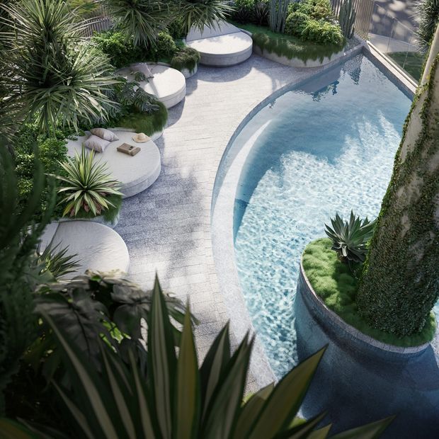 An elevated view of a landscaped courtyard pool area with a curving swimming pool, pale textured paving, rounded built-in seating platforms, and abundant sculptural tropical and drought-tolerant planting. A large cylindrical planted feature forms part of the pool edge, creating a lush, organic resort-like outdoor setting.