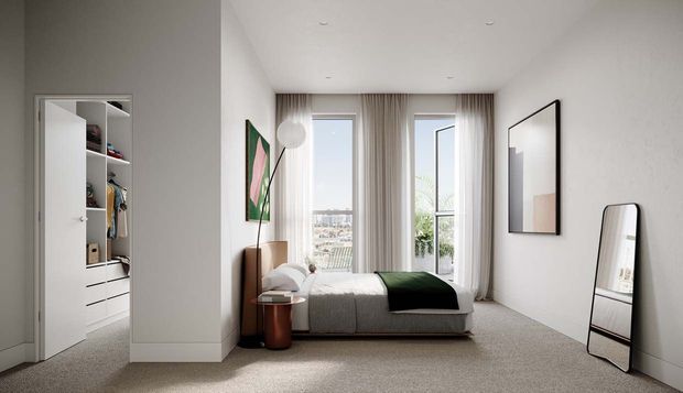 Bright contemporary bedroom with a neutral palette, a low upholstered bed, built-in open wardrobe and drawers, floor-to-ceiling sheer curtains, recessed ceiling lights, framed artwork, and a leaning full-length mirror. A balcony or exterior view is visible through the glazing.