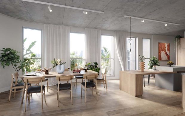 Bright open-plan contemporary interior featuring a dining area and kitchen. A timber dining table with six chairs sits beside tall windows dressed in sheer curtains, while a large timber kitchen island with dark cabinetry occupies the right side. The space has a raw concrete ceiling, pale timber flooring, abundant greenery, and a warm neutral palette with natural light.