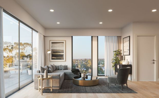 Contemporary living room with floor-to-ceiling glazing and a balcony visible to the left, a grey sectional sofa, round coffee table, accent chair, neutral rug, timber flooring, recessed ceiling lights, and framed wall art. A landscaped suburban view is visible through the windows.