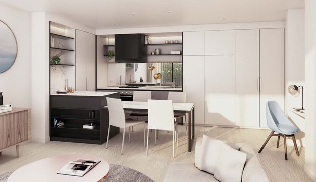 Bright, refined open-plan interior combining a compact kitchen, dining area and living space. The room features extensive white built-in cabinetry, a dark kitchen island and shelving, pale timber flooring, a white dining table with upholstered chairs, and a soft neutral lounge area. Large integrated storage and clean linear detailing create a contemporary, minimalist appearance.