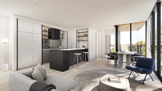 Bright open-plan contemporary apartment interior combining a minimalist kitchen, dining area and living room. The space features matte white full-height cabinetry, a dark kitchen island and shelving, pale flooring, a light grey sofa, a round textured coffee table, and floor-to-ceiling black-framed glazing opening to a balcony or outdoor view. A timber-lined ceiling detail adds warmth near the dining area.