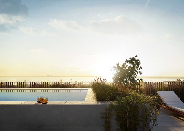 Sunlit outdoor pool terrace overlooking a calm coastal or waterfront horizon. The foreground features a dark rendered or tiled retaining wall, rectangular swimming pool, timber privacy balustrade, planted garden bed, and a reclining outdoor lounge chair. The scene has a warm, serene resort-like atmosphere.