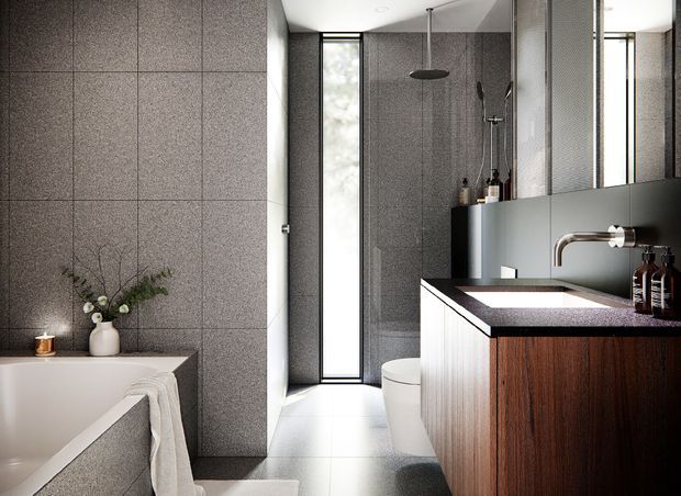 Contemporary bathroom with dark grey tiled walls, a freestanding bathtub, walk-in shower, toilet, and floating timber vanity. The vanity has a dark stone benchtop, integrated white basin, wall-mounted brushed metal tapware, and large mirrors. A narrow full-height window brings in natural light, while restrained styling creates a refined, modern atmosphere.