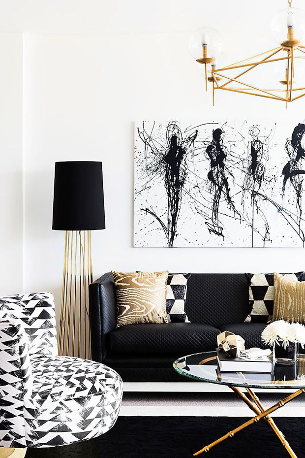 A boldly styled living room with a black quilted sofa, graphic black-and-white patterned lounge chair, monochrome abstract artwork, and geometric cushions. Gold-toned sculptural lighting and a glass coffee table add glamour, while a black-and-white rug reinforces the high-contrast scheme.