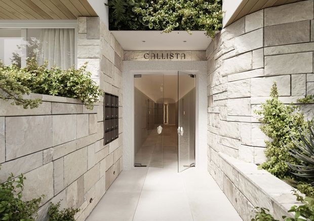 A refined apartment or commercial building entrance passage framed by pale natural stone block walls, with a glass entry door, recessed lighting, integrated planter boxes, and a lush planted feature above the doorway. The name “CALLISTA” is mounted over the entrance. Timber-look slatted soffits and restrained contemporary detailing create a calm, upscale arrival space.