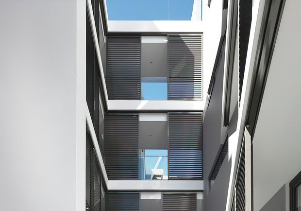A narrow multi-storey internal architectural void or courtyard with stacked levels, dark horizontal louvred screens, white walls, extensive glazing, and strong overhead daylight. The vertical composition emphasizes repeated balconies or openings and a skylit, contemporary building envelope.