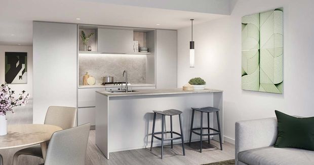 Bright open-plan contemporary kitchen and dining area with a pale grey island, integrated cabinetry, textured splashback, pendant lighting, bar stools, round dining table, and adjacent living seating. Soft neutral finishes are accented by green cushions, plants, and abstract wall art.