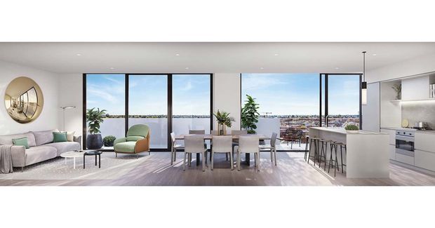 Bright open-plan apartment interior combining a living room, dining area and contemporary kitchen. Full-height black-framed glazing opens to a balcony with a broad urban or coastal outlook. The space features pale timber flooring, white cabinetry and walls, a light sofa, green accent chairs, a dining table, and a white kitchen island with bar seating.
