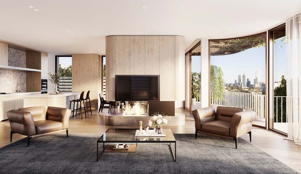 A bright, refined open-plan living room with a contemporary kitchen and dining area. The space features a curved light timber fireplace wall with an inset television and linear firebox, neutral upholstered and leather seating, a dark textured rug, low coffee table, and expansive glazed doors opening to a balcony with a city skyline view.