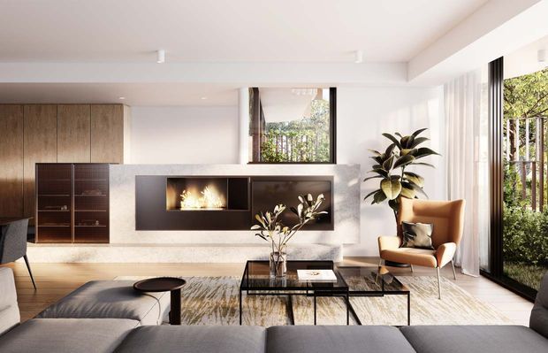 Bright contemporary living room with a low-profile sectional sofa, black glass coffee tables, a sculptural armchair, timber built-in cabinetry, and a feature fireplace set into a pale stone or plaster wall. Full-height glazing and a glazed door open to lush greenery, while large indoor plants and neutral furnishings create a refined, warm atmosphere.