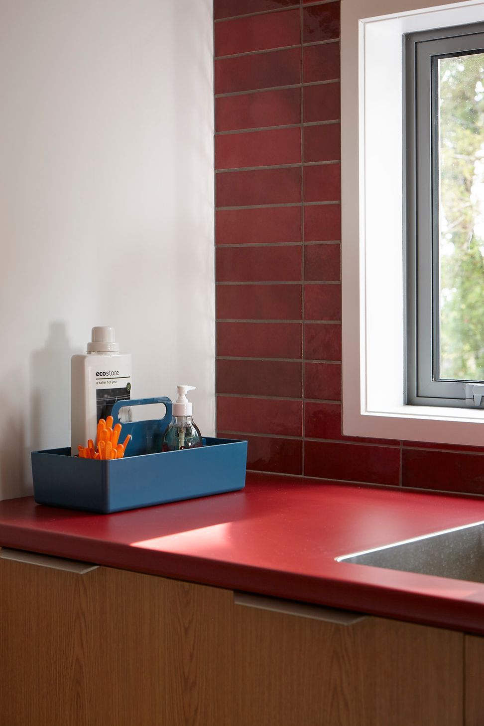 A close-up of the laundry highlights the playful use of colour and carefully crafted joinery. Red Formica surfaces, oak cabinetry and textured tiles elevate this everyday utility space.
