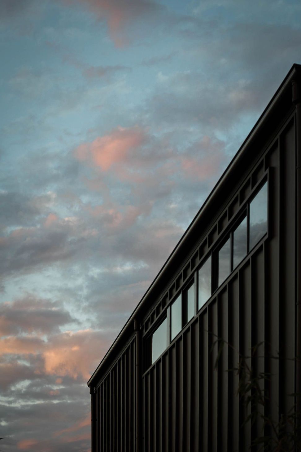 Anderson Residence - Exterior. Dark cladding and glazing against a pink evening sky.