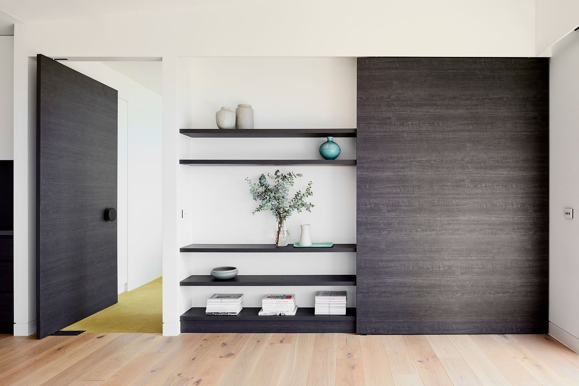 The dark veneer continues across the end wall of the Dining Room incorporating a large pivot door to the Master Suite and a concealed study nook – the green carpet of the bedroom echoing the cellar below.