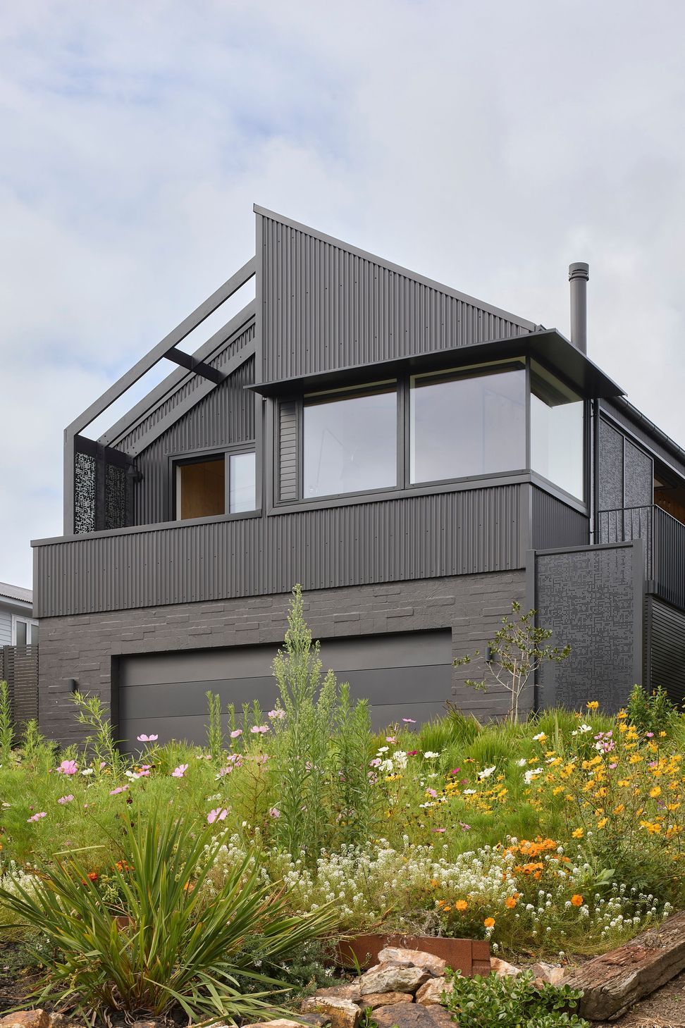 Viewed from the garden, the front elevation presents a simple architectural form clad in black corrugated metal. Native planting softens the building and strengthens its connection to the landscape.