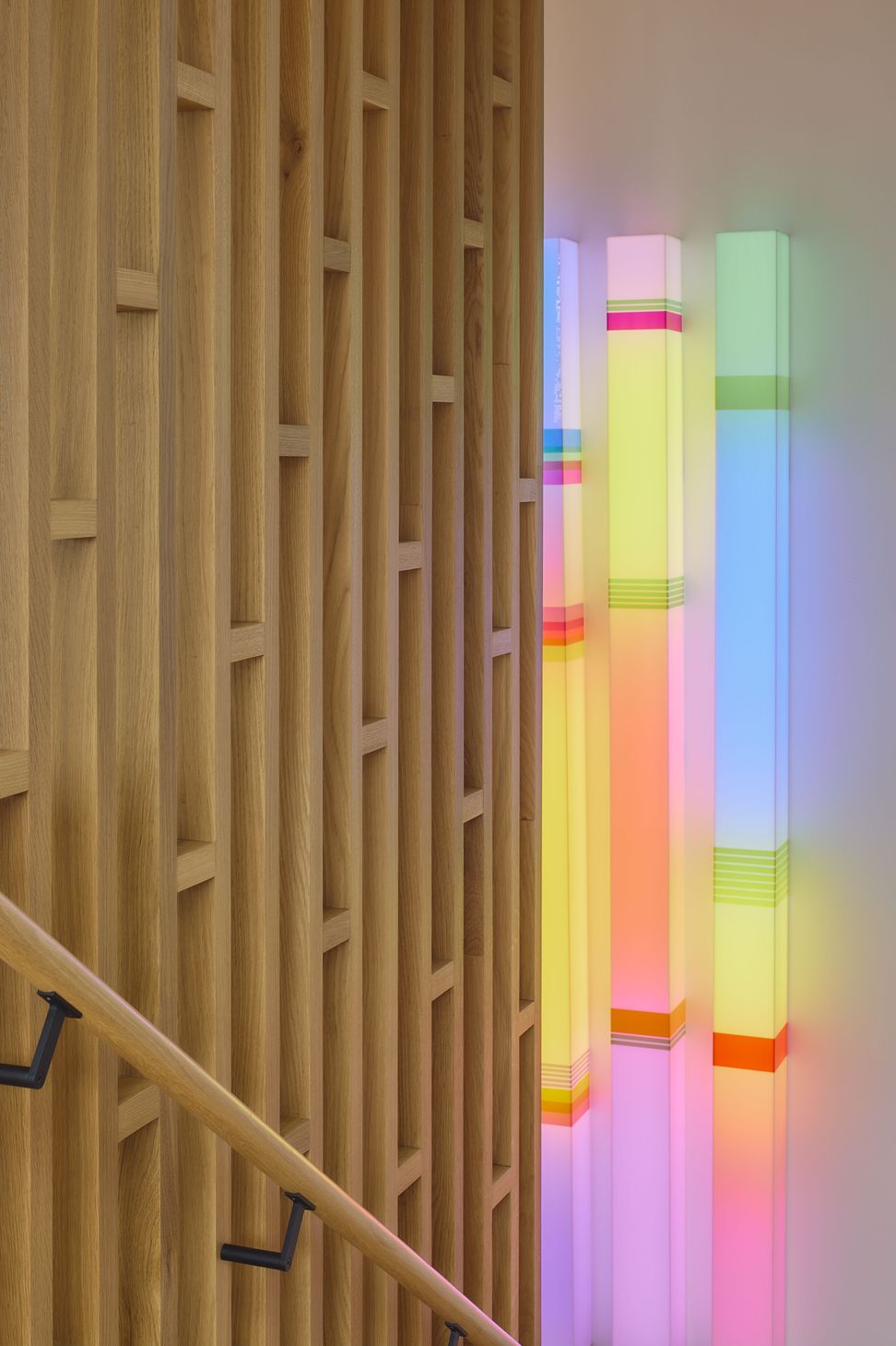 The staircase is screened by a contemporary timber feature wall that filters light and views. A vibrant linear lightbox artwork introduces colour and personality to the circulation space.