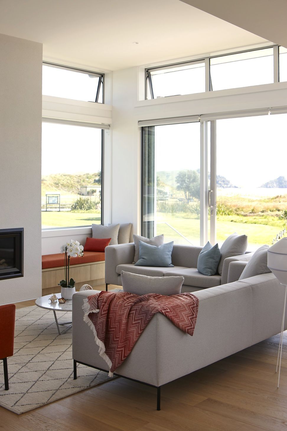 The living room combines warm oak flooring with crisp white walls and ceilings to create a calm coastal interior. Expansive aluminium sliding doors and clerestory glazing frame uninterrupted ocean views while filling the space with natural light.