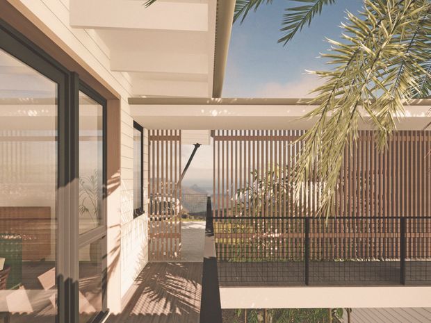 A sunny modern outdoor terrace or balcony beside a light-coloured rendered and timber-clad building. The space features large dark-framed glazed doors, a covered pergola, vertical timber privacy screens, dark metal balustrading, and palm planting, with a distant landscape visible beyond.