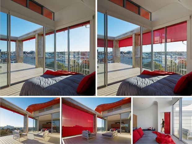 A collage of a contemporary waterfront apartment interior and terrace. The bedroom and adjoining living area feature full-height glazing, exposed concrete columns, pale flooring, white curved ceilings, and vivid red roller blinds and soft furnishings. Marina and urban waterfront views are visible through the glazing, with outdoor seating on the terrace.