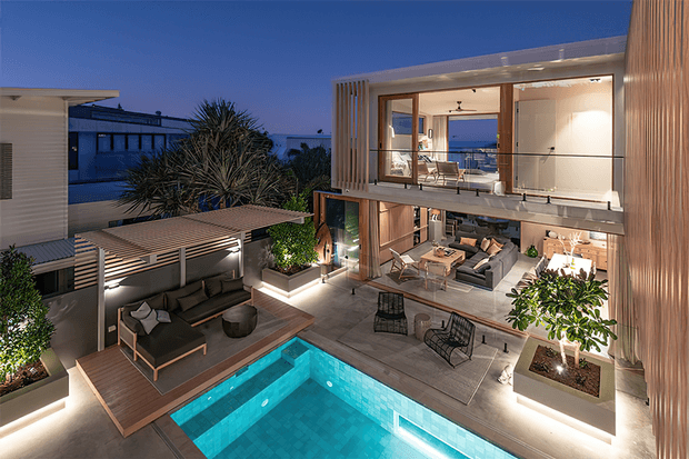 Twilight exterior view of a contemporary multi-level residence organized around a rectangular swimming pool and landscaped terrace. The home features extensive floor-to-ceiling glazing, warm timber-toned vertical cladding, a covered outdoor lounge, illuminated planters, and an open-plan living area visible through the glass.