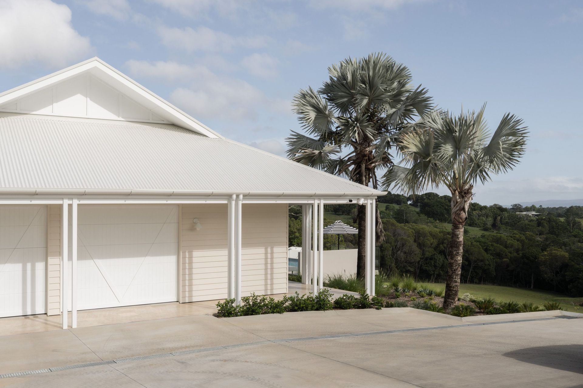 Euroa Farm - Exterior. Gabled garage and verandah framed by palms and hinterland views.