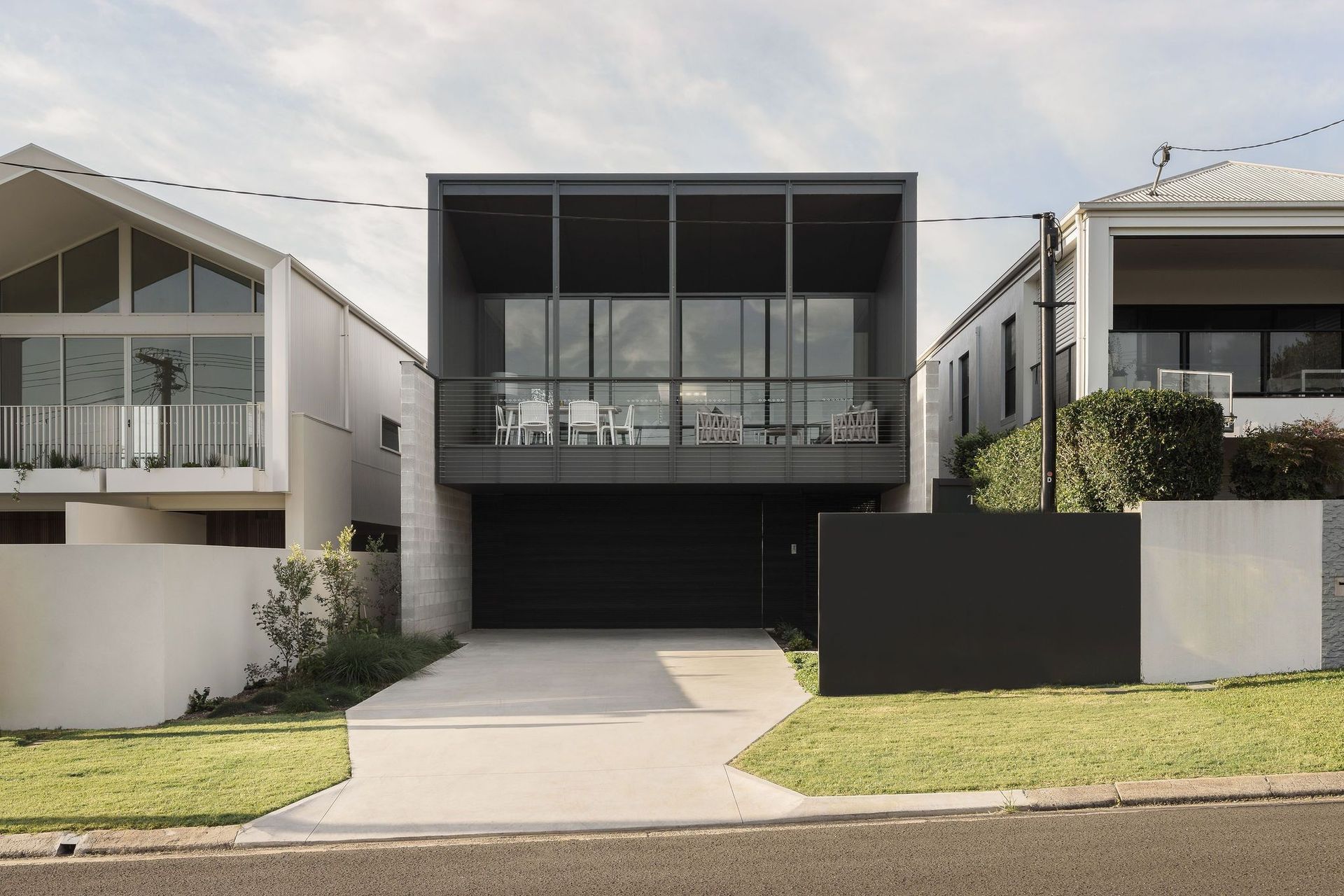 Gilbert Residence - Exterior. Front elevation with balconies, dark cladding and a landscaped frontage.