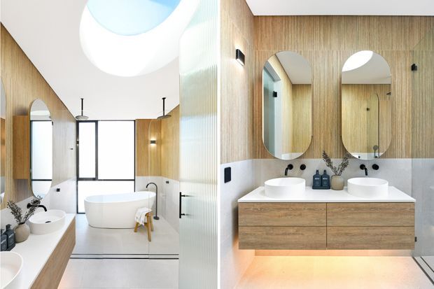Bright contemporary bathroom featuring a freestanding bathtub, double floating timber vanity with two vessel basins, rounded mirrors, pale stone or tile wall surfaces, vertical timber wall panelling, black tapware and fixtures, and a large circular skylight. The composition shows both the main bathing area and the double vanity.
