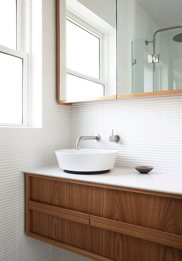 Bright contemporary bathroom featuring a floating dark timber vanity with integrated drawers, a white vessel basin, wall-mounted chrome tapware, white horizontal wall tiling, and a large mirrored cabinet with timber trim. A glazed shower enclosure is visible in the reflection.