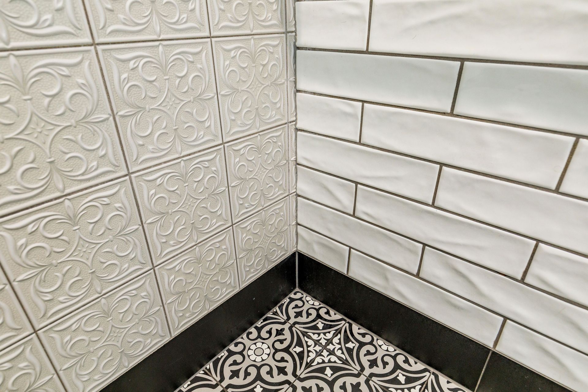 In this black &amp; white bathroom the goal was to create a traditional charm. The floor tiles are Tile Warehouse - Element - Arabesque with the skirt tile Tile Warehouse -Pure Black Matt. The textured subway tiles are Tile Space - MT1366 - Marlow Cloud Gloss and the decorative antique embossed pattern tile is Tile Depot - Antigua Muse White.