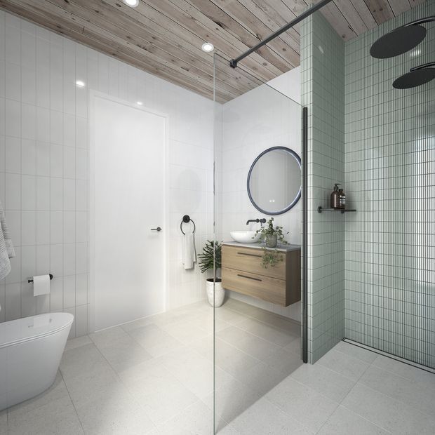Bright contemporary bathroom with a frameless glass shower enclosure, pale grey floor and wall tiles, a sage-green small-format tiled feature wall, floating timber vanity with white basin, round mirror, wall-mounted fixtures, and a light timber-lined ceiling.