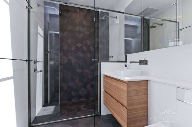 Contemporary bathroom with a frameless glass walk-in shower, dark geometric feature tile wall and floor, white walls, large mirror, wall-mounted chrome tapware, and a floating timber vanity with a white vessel basin.