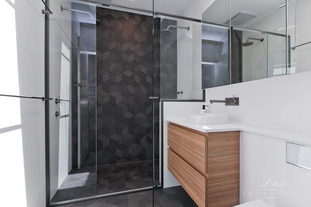 Contemporary bathroom featuring a frameless glass walk-in shower, dark geometric feature tiles on the shower wall and floor, white tiled walls, a floating timber vanity with integrated drawers, a white vessel basin, wall-mounted chrome tapware, and a large mirrored wall.