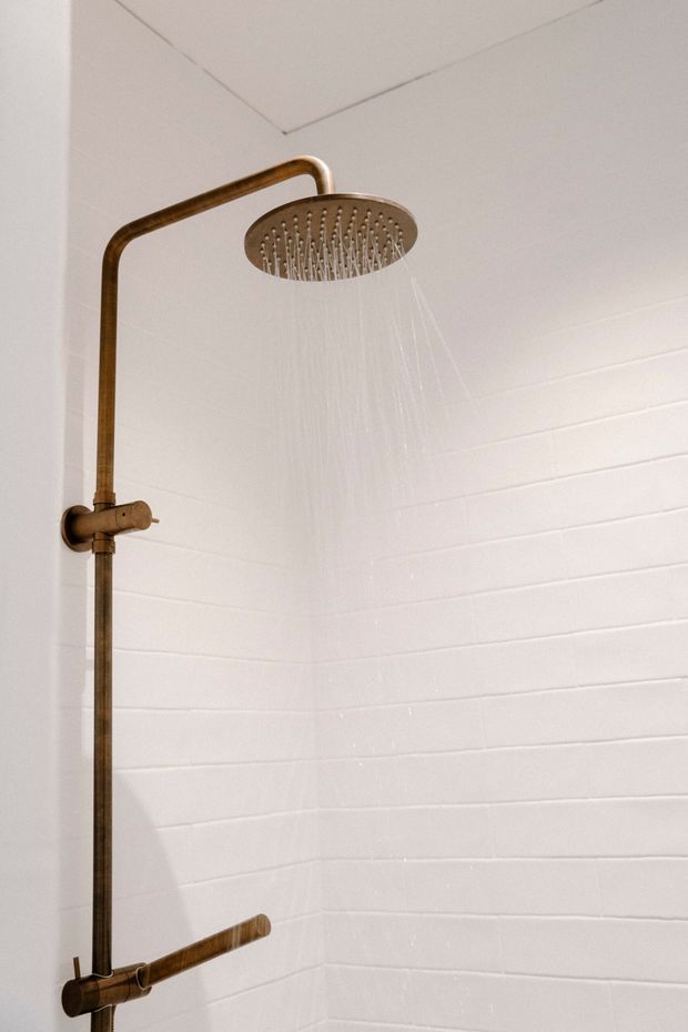 Close-up of a contemporary shower enclosure featuring white horizontal wall tiles and a bronze/brass-finished exposed shower system with a large round rain showerhead and matching controls.