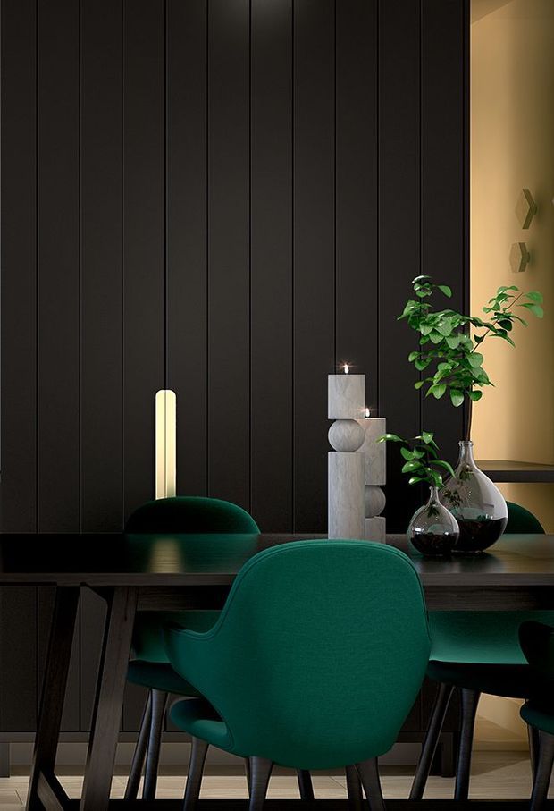 Moody, refined dining area featuring a dark vertically panelled wall, a black dining table, and deep emerald-green upholstered dining chairs. Warm integrated lighting, sculptural candles, and glass vases with leafy greenery create a sophisticated contemporary atmosphere.