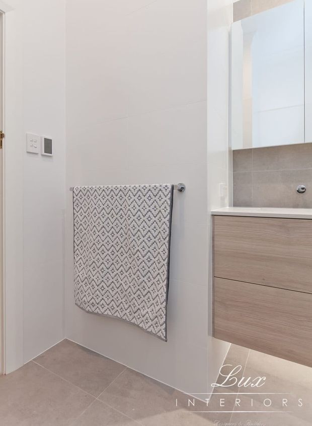 Bright, compact contemporary bathroom featuring large light neutral wall and floor tiles, a floating light-wood vanity with integrated countertop, a large mirrored cabinet, chrome fittings, and a patterned towel on a wall-mounted rail.