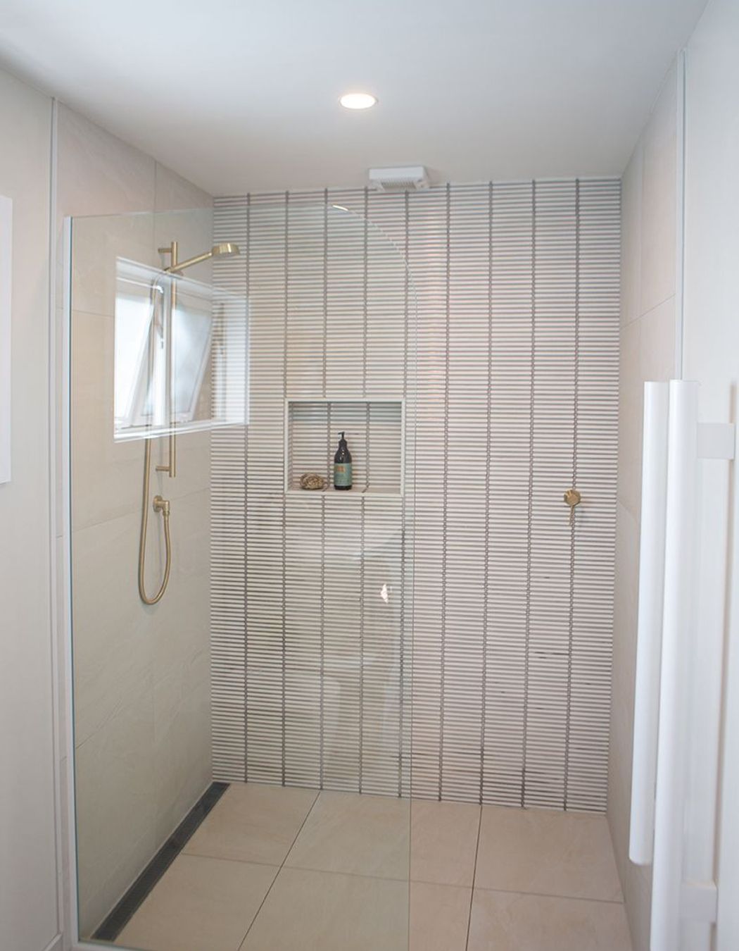 Generous shower with brass slide shower, recessed niche and a simple fixed glass pane.