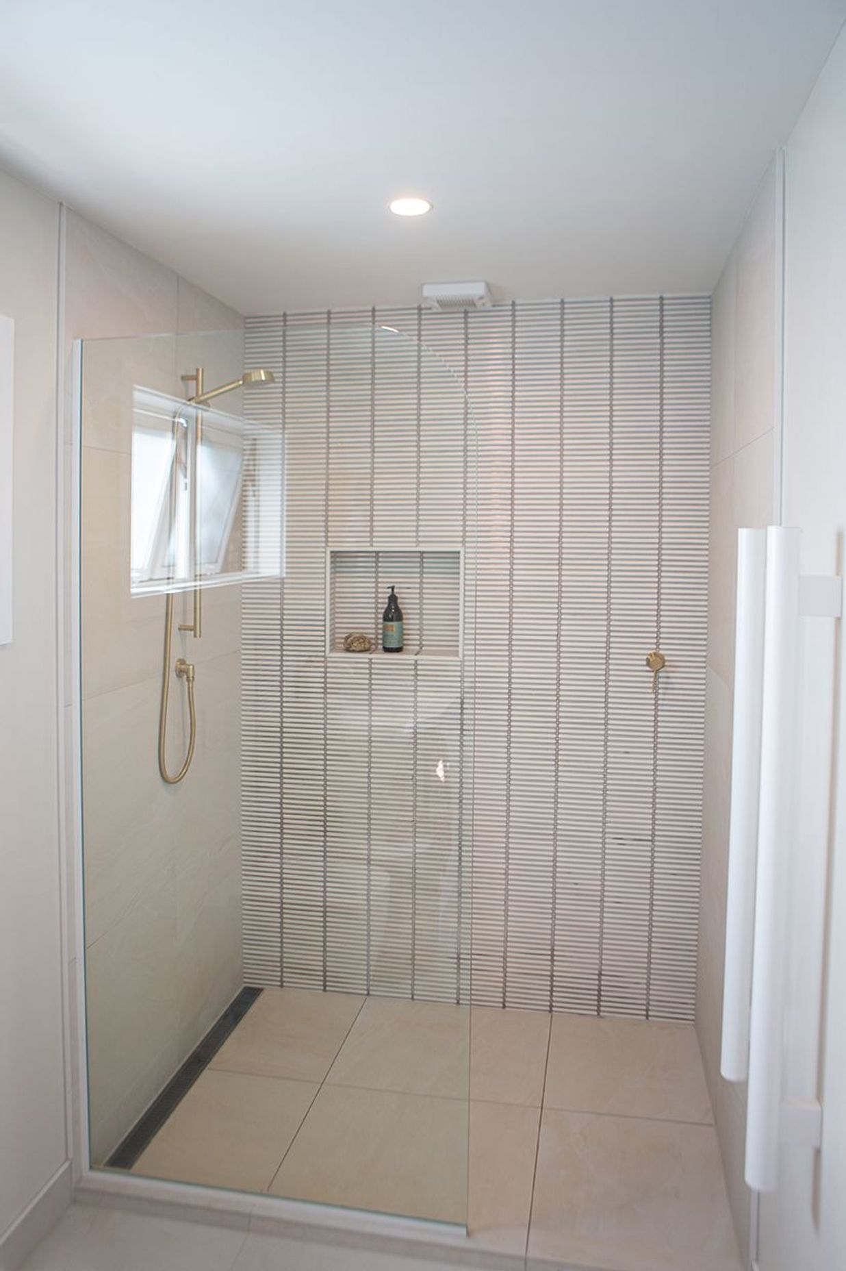 Generous shower with brass slide shower, recessed niche and a simple fixed glass pane.