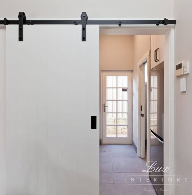 Bright transitional entry hall featuring a large white paneled sliding barn door on a black metal track, opening toward a narrow tiled corridor with a glazed exterior door, white trim, and built-in cabinetry.