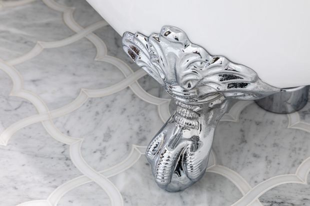 Close-up detail of an ornate polished chrome clawfoot bathtub foot resting on a pale grey and white marble-patterned floor with curved decorative inlay.