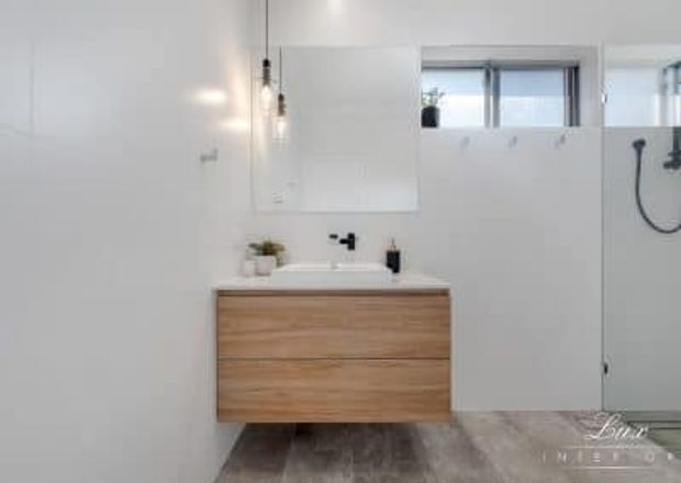 Bright contemporary bathroom featuring a floating timber-veneer vanity with white basin and black tapware, a large mirrored cabinet, white wall finishes, a high horizontal window, and a glass shower enclosure with black fittings. Grey-toned flooring and minimal pendant lighting complete the clean, modern scheme.