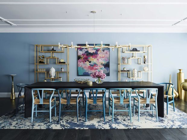 A refined dining room with a long dark dining table surrounded by blue-toned chairs, set against a pale blue wall. Gold-toned open shelving displays decorative objects on either side of a colourful abstract artwork. A linear contemporary chandelier hangs above the table, while a patterned area rug and dark timber flooring ground the space. The room combines polished modern furnishings with decorative, art-led styling.